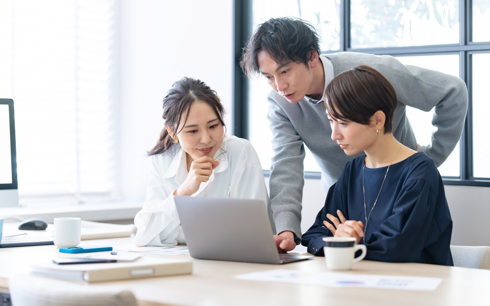 明るいオフィスで若手エンジニアがモニターを囲んで話し合っている様子のイメージ写真